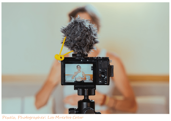 Image of entrepreneur blurred with camera in focus talking to camera- recording her video.